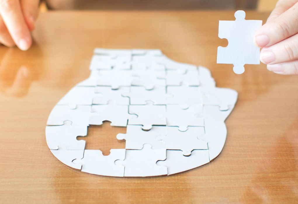 Puzzleteile formen ein Gehirn, ein Teil wird von Hand eingesetzt.