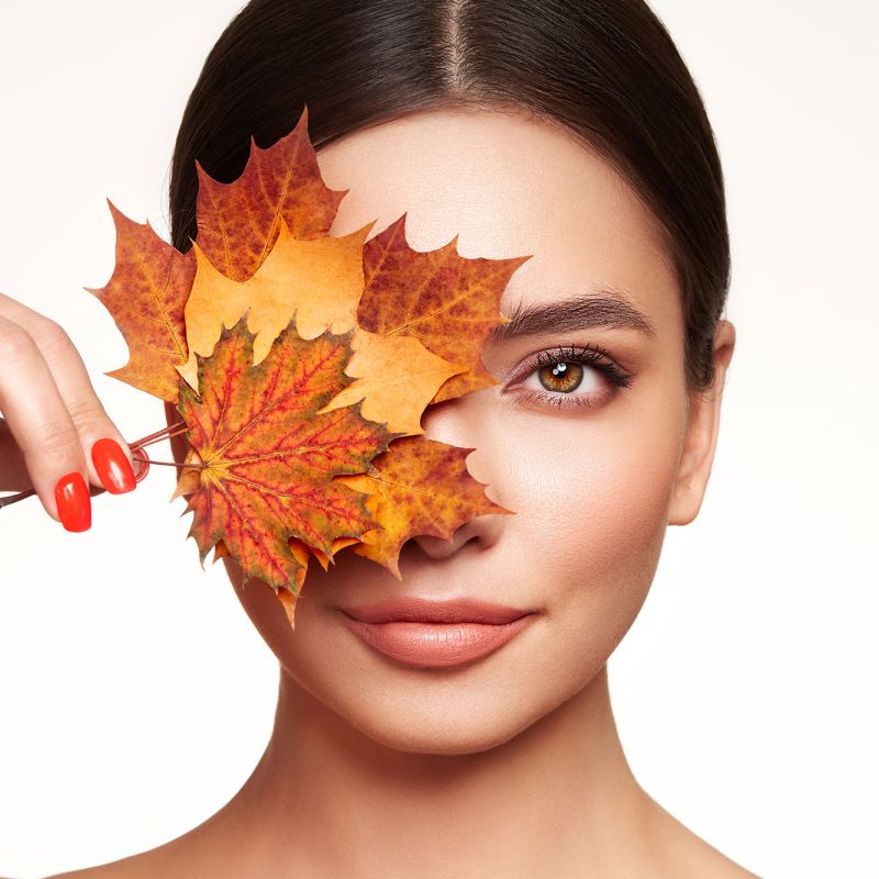 Frau mit Herbstblättern vor dem Gesicht, Symbol Hautpflege