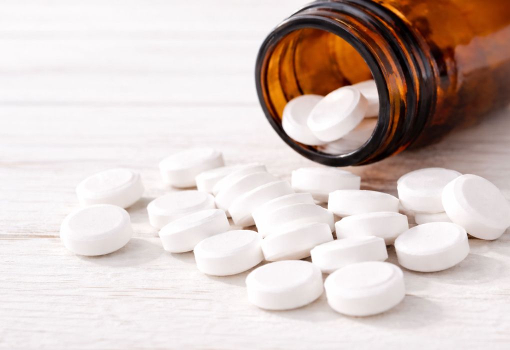 Weiße Tabletten liegen neben einer geöffneten braunen Glasflasche auf hellem Untergrund