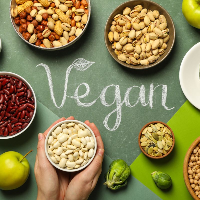 Verschiedene pflanzliche Lebensmittel um das Wort „Vegan“ auf grünem Hintergrund angeordnet