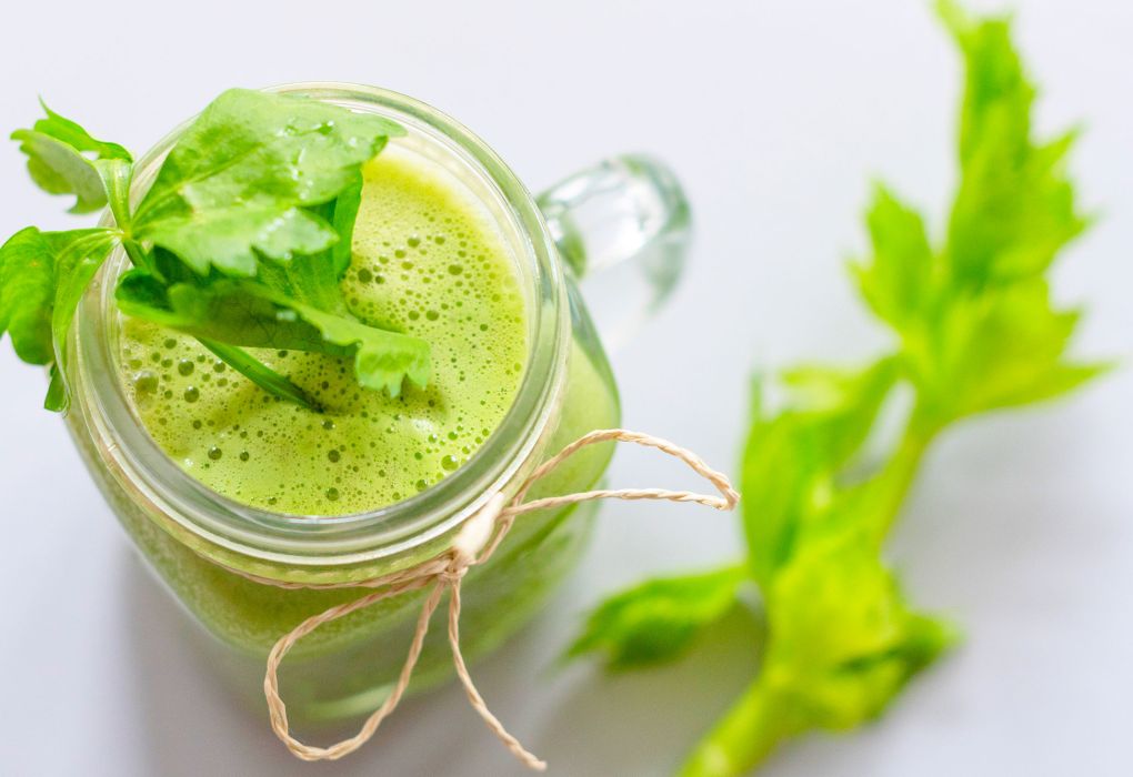 Glas mit grünem Smoothie, Selleriestangen daneben auf hellem Hintergrund
