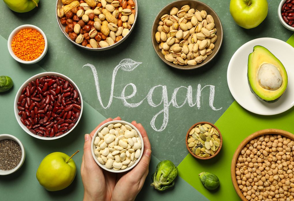 Verschiedene pflanzliche Lebensmittel um das Wort „Vegan“ auf grünem Hintergrund angeordnet
